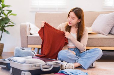 Genç bir kadın yerde oturuyor, valizini düzenlerken paketleme listesindeki eşyaları kontrol ediyor, her şeyin yolunda olduğundan emin oluyor..