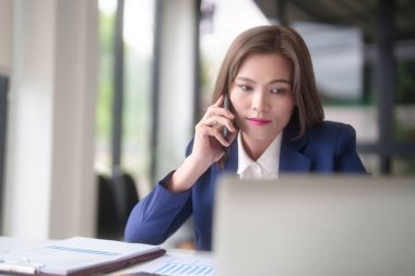 Asyalı iş kadınları iş arkadaşlarıyla konuşmak için akıllı telefon kullanıyor ve iş verilerini araştırmak için klavye bilgisayarında yazı yazarken ofis dışındaki yeni girişimlerin yatırım ve pazar stoklarını analiz ediyorlar..