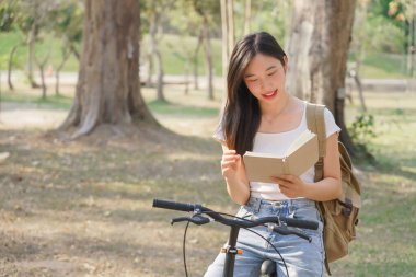 Sırt çantalı genç Asyalı kadınlar bisiklete binip mutlu bir şekilde kitap okuyorlar. Bisiklet sürdükten sonra dinleniyorlar..