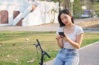 Bisikletli genç Asyalı kadınlar mesaj okumak için bisiklet sürerken sohbet ediyorlar ve bisiklet sürdükten sonra akıllı telefondan sosyal medyayı kontrol ediyorlar..