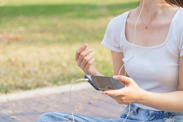 Closeup of young asian women wearing earphone and listening music on smartphone with happiness while sitting on the street to relaxation with journey travel lifestyle after cycling bicycle in park.