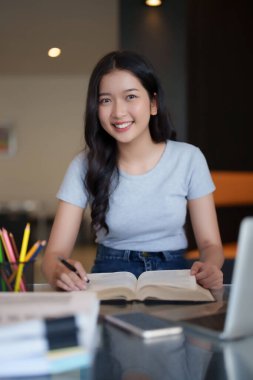 Asyalı genç kız öğrenci kitap yazmak ve ödev yapmak için kitap okuyor. İnternette bilgisayar dersi izledikten ve kafede eğitim bilgisi öğrendikten sonra ödev yapıyor..