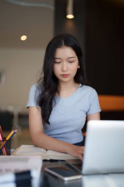 Bir kitap okuduktan sonra ödev yapmak için dizüstü bilgisayarda yazı yazan ve araştırma yapan Asyalı genç kız öğrenci kafe 'de eğitim bilgisi üzerine online dersler izledi..