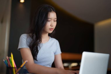 Bir kitap okuduktan sonra ödev yapmak için dizüstü bilgisayarda yazı yazan ve araştırma yapan Asyalı genç kız öğrenci kafe 'de eğitim bilgisi üzerine online dersler izledi..