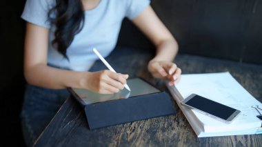 Asyalı genç kız öğrenci internetten eğitim bilgisini öğrenme ve öğrenme dersleri alırken aynı zamanda bir kitap okuyor ve kafedeki dijital tablet ödevi hakkında notlar alıyor..