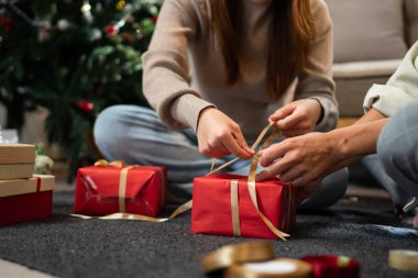 Genç bir çift yerde oturuyor, Noel hediyelerini paketliyorlar. Sahne şenlikli dekorasyonlar ve hediyelerle dolu. Sıcak bir tatil ortamı yaratıyor..