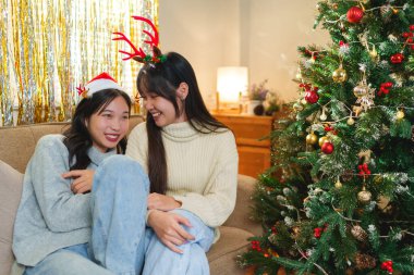 İki arkadaş, süslü bir Noel ağacının yanında oturmuş geyik boynuzları takıp gülerek neşeli ve neşeli bir atmosfer yaratıyorlar..