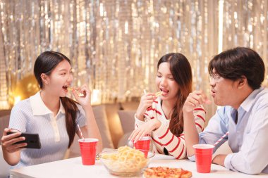 Neşeli bir grup arkadaş, eğlence dolu bir doğum günü partisinde birlikte selfie çekiyorlar. Etrafı abur cuburlar, içkiler ve şenlikli bir arka planla çevrili..