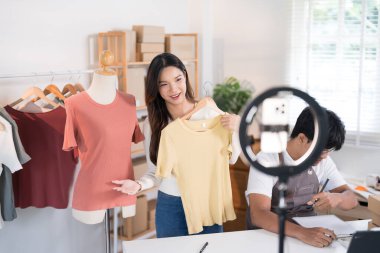 Bir kadın, yoğun bir ekolojik çalışma alanında dizüstü bilgisayar üzerinde çalışırken, canlı yayın sırasında mankenin üstünde bir gömlek sunar..