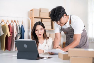 Bir erkek ve kadın, online bir iş yerinde kağıt ve dizüstü bilgisayar siparişlerini doğrulamak için birlikte çalışırlar..