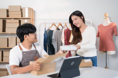  Bir adam, kargo kutuları ve elbise raflarıyla dolu bir çalışma alanında bir kadına düzgün paketlenmiş bir paket verir..