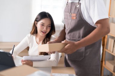 Bir erkek, bir kadın elbise askısı ve nakliye malzemeleriyle telefonuna bakarken bir kutu hazırlar..