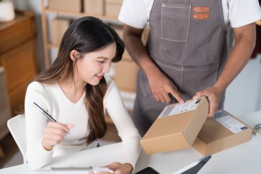 Bir erkek, bir kadın elbise askısı ve nakliye malzemeleriyle telefonuna bakarken bir kutu hazırlar..