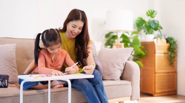 Kitap ve kırtasiye malzemeleriyle çevrili, öğrenim ve desteği destekleyen bir anne, yemek masasında kızına yardım ediyor..