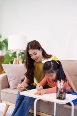 Kitap ve kırtasiye malzemeleriyle çevrili, öğrenim ve desteği destekleyen bir anne, yemek masasında kızına yardım ediyor..