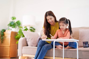 Kitap ve kırtasiye malzemeleriyle çevrili, öğrenim ve desteği destekleyen bir anne, yemek masasında kızına yardım ediyor..