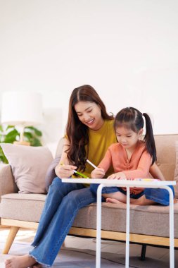 Kitap ve kırtasiye malzemeleriyle çevrili, öğrenim ve desteği destekleyen bir anne, yemek masasında kızına yardım ediyor..