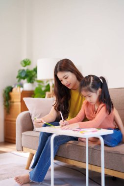 Kitap ve kırtasiye malzemeleriyle çevrili, öğrenim ve desteği destekleyen bir anne, yemek masasında kızına yardım ediyor..