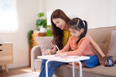 Kitap ve kırtasiye malzemeleriyle çevrili, öğrenim ve desteği destekleyen bir anne, yemek masasında kızına yardım ediyor..
