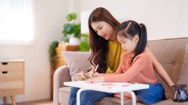 Kitap ve kırtasiye malzemeleriyle çevrili, öğrenim ve desteği destekleyen bir anne, yemek masasında kızına yardım ediyor..