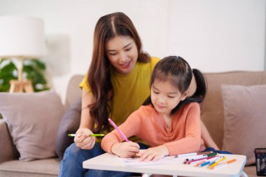 Kitap ve kırtasiye malzemeleriyle çevrili, öğrenim ve desteği destekleyen bir anne, yemek masasında kızına yardım ediyor..