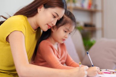 Kitap ve kırtasiye malzemeleriyle çevrili, öğrenim ve desteği destekleyen bir anne, yemek masasında kızına yardım ediyor..