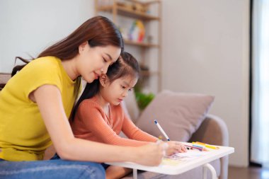 Kitap ve kırtasiye malzemeleriyle çevrili, öğrenim ve desteği destekleyen bir anne, yemek masasında kızına yardım ediyor..
