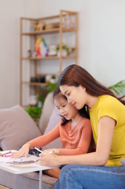 Kitap ve kırtasiye malzemeleriyle çevrili, öğrenim ve desteği destekleyen bir anne, yemek masasında kızına yardım ediyor..