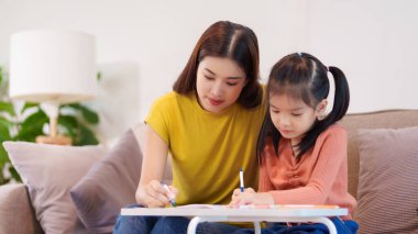 Kitap ve kırtasiye malzemeleriyle çevrili, öğrenim ve desteği destekleyen bir anne, yemek masasında kızına yardım ediyor..