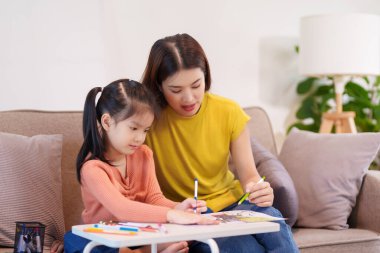 Kitap ve kırtasiye malzemeleriyle çevrili, öğrenim ve desteği destekleyen bir anne, yemek masasında kızına yardım ediyor..