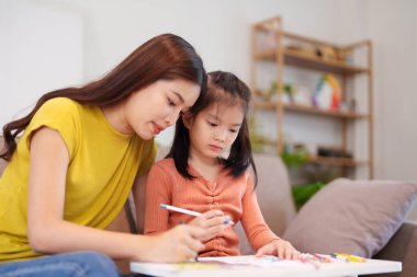 Kitap ve kırtasiye malzemeleriyle çevrili, öğrenim ve desteği destekleyen bir anne, yemek masasında kızına yardım ediyor..