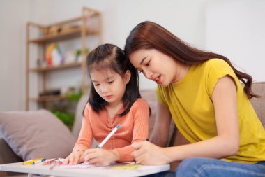 Kitap ve kırtasiye malzemeleriyle çevrili, öğrenim ve desteği destekleyen bir anne, yemek masasında kızına yardım ediyor..