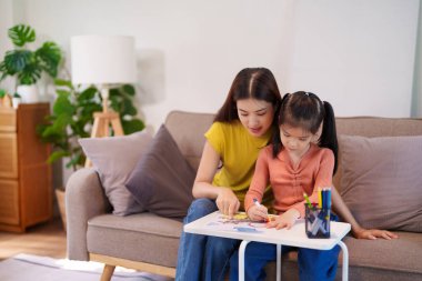 Kitap ve kırtasiye malzemeleriyle çevrili, öğrenim ve desteği destekleyen bir anne, yemek masasında kızına yardım ediyor..