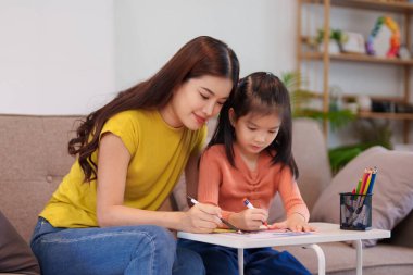 Kitap ve kırtasiye malzemeleriyle çevrili, öğrenim ve desteği destekleyen bir anne, yemek masasında kızına yardım ediyor..