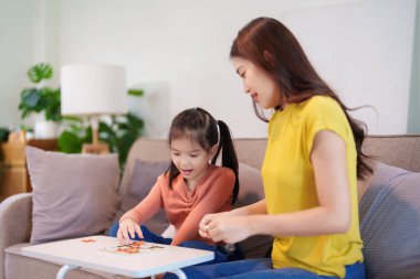  Bir anne ve kızı, bir masada birlikte oynaşarak eğleniyor, kahkahaları ve bağlantıları paylaşıyor..
