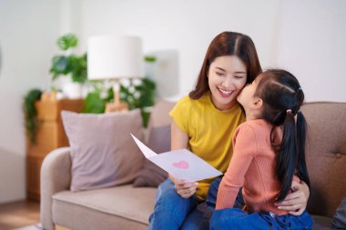 Kızlarının el yapımı kartlarının dokunduğu anne ona sevgiyle sarılıyor ve aralarındaki güçlü duygusal bağı gösteriyor..