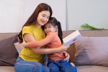 Anne, düşünceli bir el yapımı kart aldıktan sonra kızını sıcak bir şekilde kucaklıyor ve o anın tadını çıkarıyor..