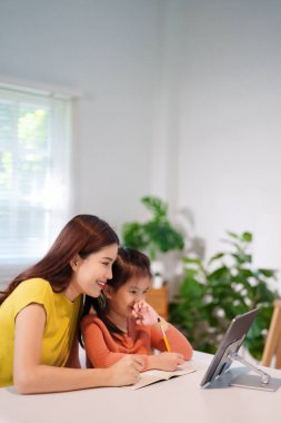 Bir anne küçük kızına masada birlikte ödev yapmayı öğretiyor, destekleyici ve eğitici bir ortam yaratıyor..