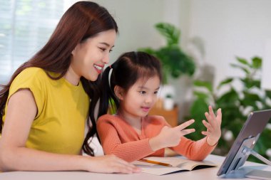 Bir anne küçük kızına masada birlikte ödev yapmayı öğretiyor, destekleyici ve eğitici bir ortam yaratıyor..