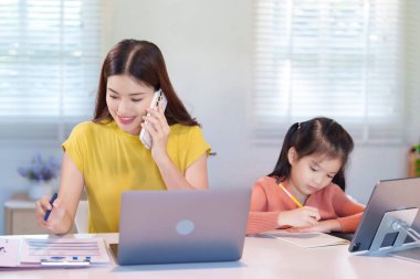 Bir anne ve kızı masada birlikte ödev yapıyorlar, araştırma için bir dizüstü bilgisayar kullanıyorlar..
