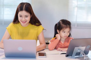 Bir anne ve kızı masada birlikte ödev yapıyorlar, araştırma için bir dizüstü bilgisayar kullanıyorlar..