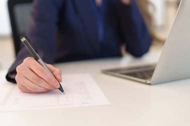 Ofis masasında notlar alırken Asyalı genç bir iş kadınının telefonla konuşmasının yakın çekimi.