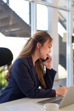 Ofis masasında sanal bir toplantı yaparken Asyalı genç bir iş kadını telefonda konuşuyor.