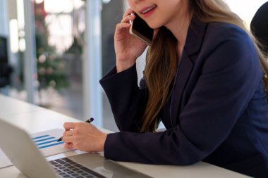 Ofis masasında sanal bir toplantı yaparken Asyalı genç bir iş kadını telefonda konuşuyor.