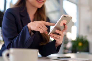 Parlak ve modern bir ofiste çalışırken akıllı telefon kullanan Asyalı genç bir iş kadınının yakın çekimi.