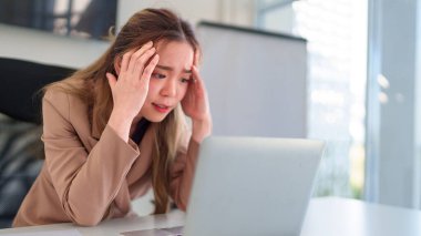 Genç Asyalı iş kadını dizüstü bilgisayarına bakıp iş yerindeki sorunları analiz ederken stresli hissediyor