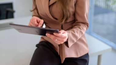 Parlak ve modern ofis ortamında tablet kullanırken gülümseyen genç Asyalı iş kadını