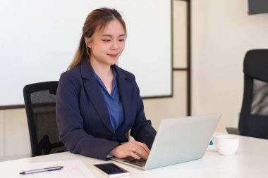 Genç Asyalı iş kadını ofis masasında bilgisayarla çalışıyor. Temiz ve düzenli bir çalışma alanında.