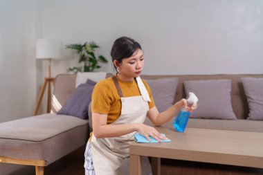 Asyalı bir hizmetçinin, ahşap bir masayı sprey şişe ve mikrofiber bezle temizlerken yakın plan fotoğrafı.