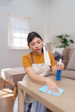 Asyalı bir hizmetçinin, ahşap bir masayı sprey şişe ve mikrofiber bezle temizlerken yakın plan fotoğrafı.